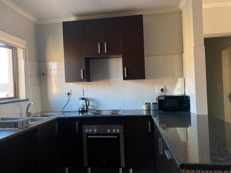 A functional kitchen featuring dark wood cabinetry, granite countertops, a built-in oven, electric hob, and a tiled backsplash.