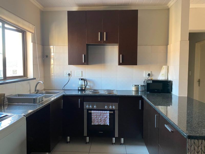 A functional kitchen featuring dark wood cabinetry, granite countertops, a built-in oven with electric hob, and a tiled backsplash.