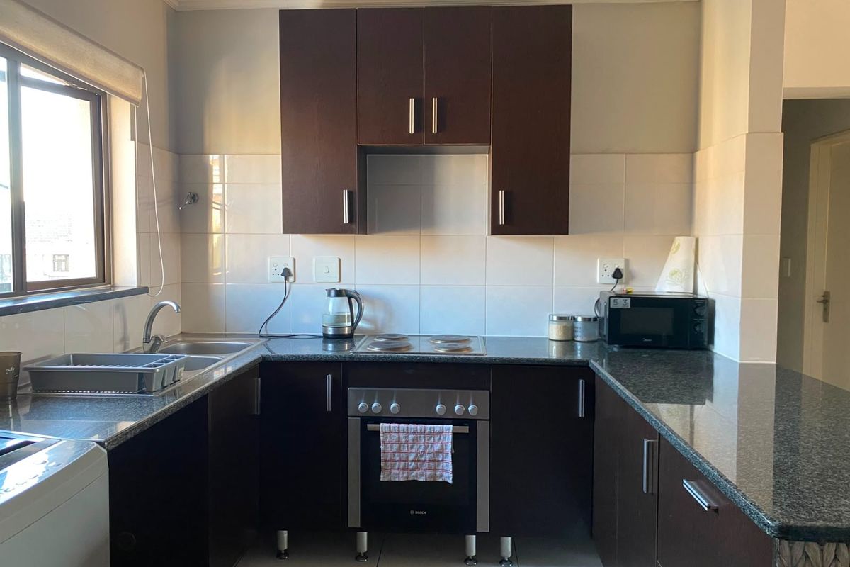 A functional kitchen featuring dark wood cabinetry, granite countertops, a built-in oven with electric hob, and a tiled backsplash.