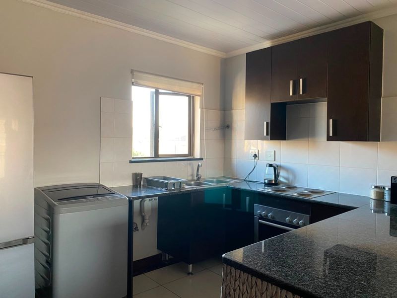 A functional kitchen featuring dark wood cabinetry, granite countertops, a built-in oven, and a tiled backsplash with ample natural light.