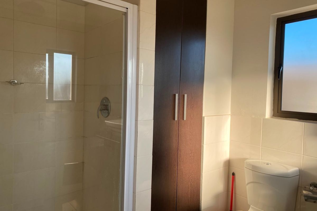 A clean, functional bathroom featuring a shower enclosure, a built-in storage cupboard, and a toilet with tiled wall finishes.