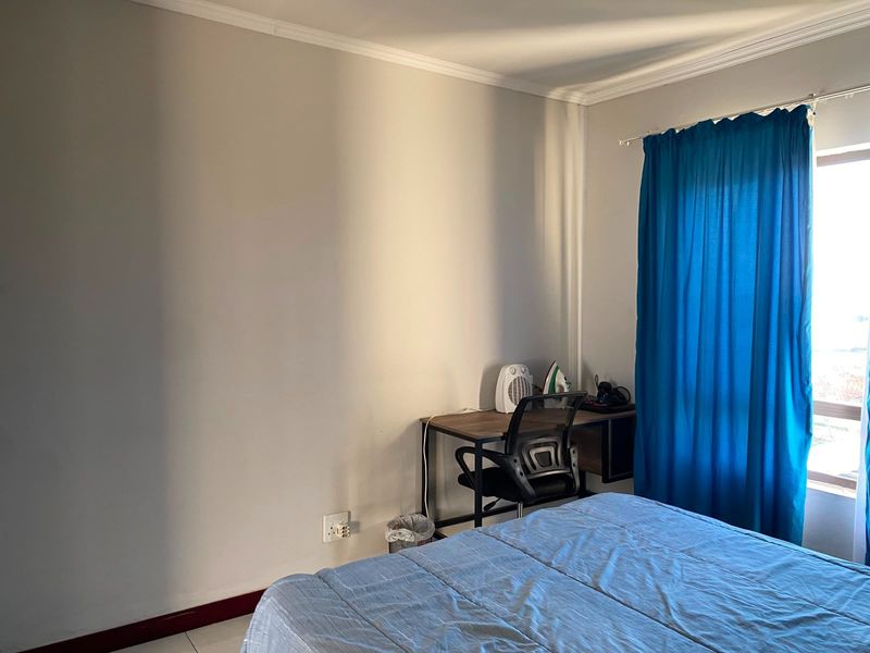 A bedroom featuring neutral walls, coving, and skirting boards, with natural light entering through a window dressed with blue curtains.