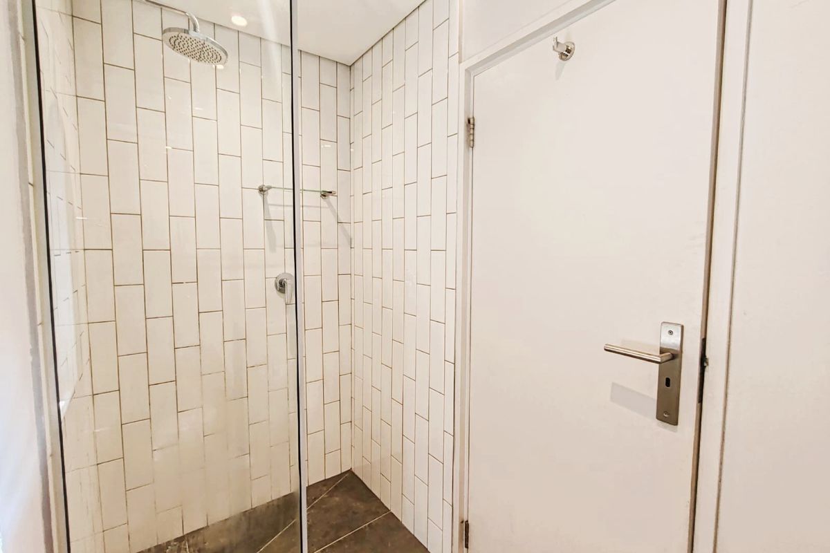 A clean, modern bathroom featuring a walk-in shower with a glass screen, rain shower head, and white subway wall tiling.