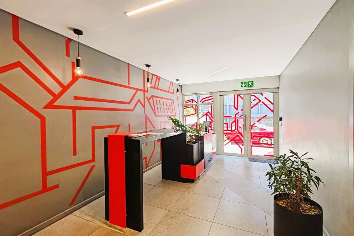 Modern apartment building entrance lobby featuring tiled flooring, a contemporary reception desk, and glass entrance doors with decorative wall graphics.