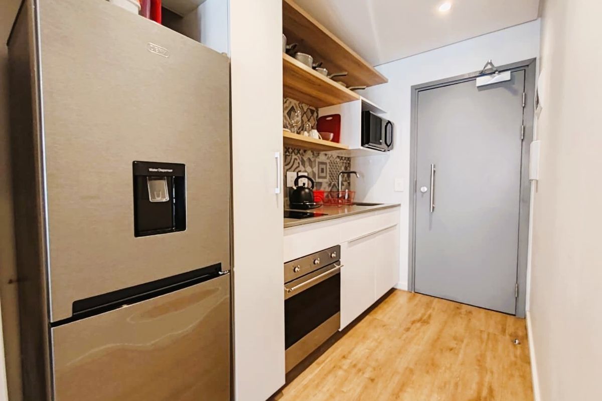 Compact modern kitchen featuring built-in oven, hob, stainless steel sink, and open shelving with patterned tile backsplash and light wood-look flooring.