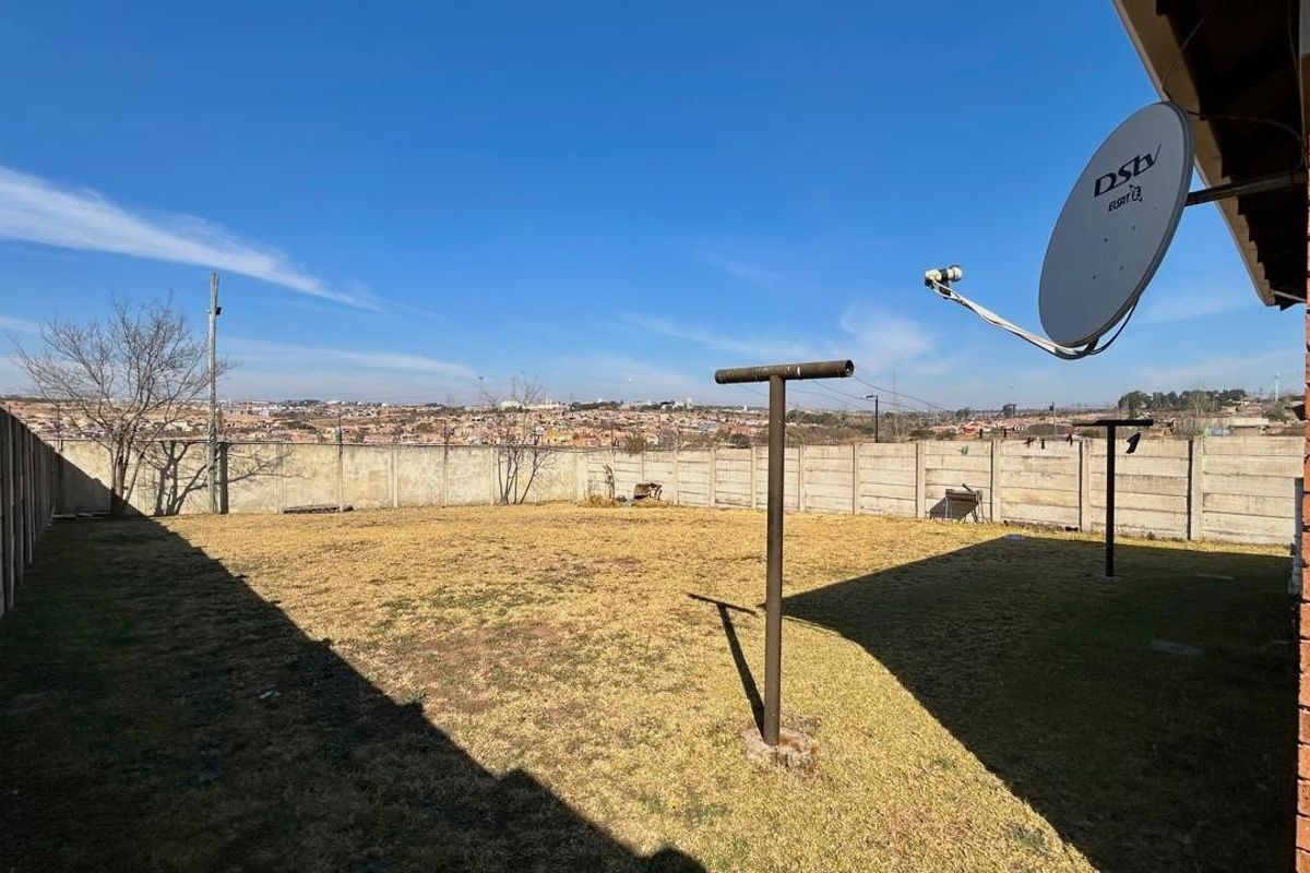 A spacious rear garden featuring a precast concrete boundary wall, a satellite dish, and a metal washing line pole with views of the surrounding area.