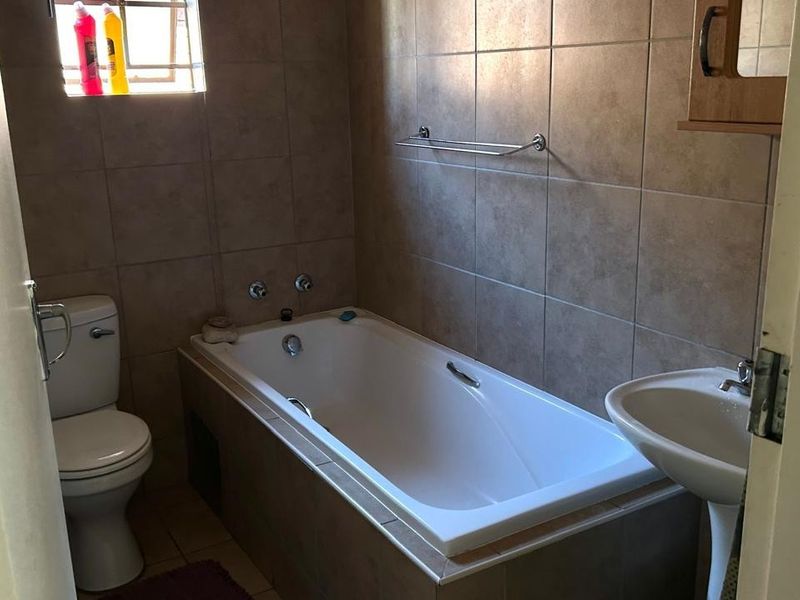 A functional bathroom featuring a bathtub, pedestal basin, toilet, and neutral wall tiling, providing a clean and practical space.