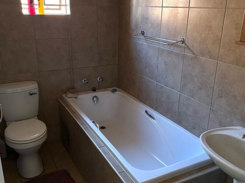 A functional bathroom featuring a built-in bathtub, pedestal washbasin, and toilet with neutral ceramic wall tiling.