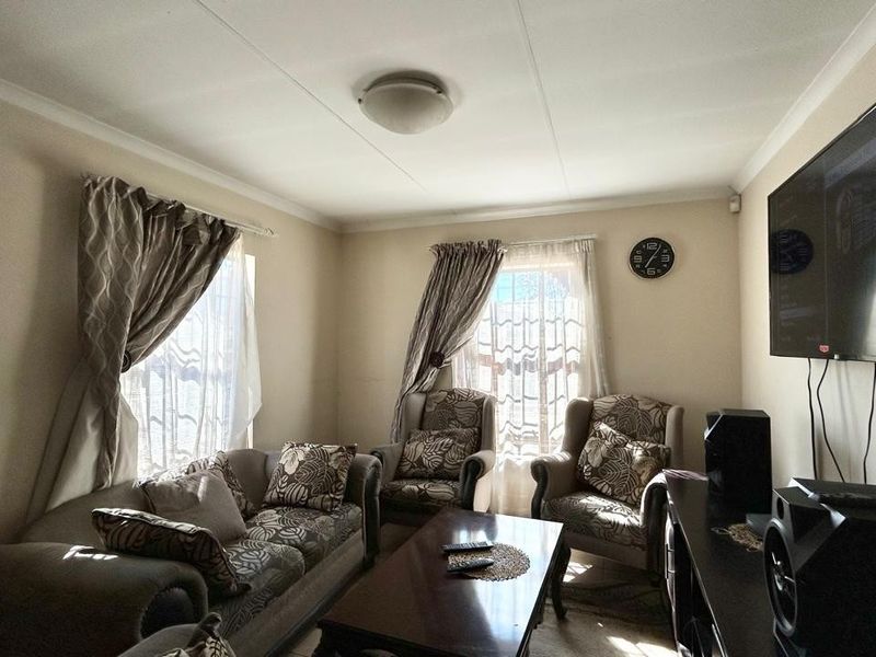 A comfortable living room featuring neutral wall tones, ceiling cornicing, and natural light through dual windows.