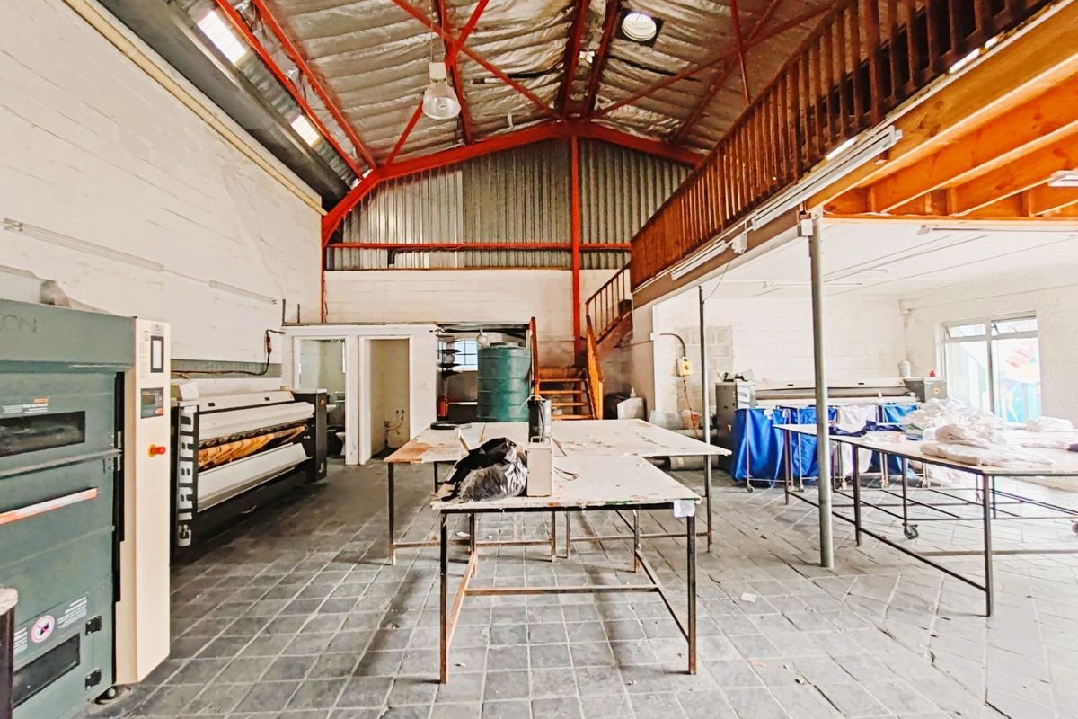Industrial utility space featuring high ceilings with exposed steel trusses, a mezzanine level, and tiled flooring, currently utilized for commercial laundry operations.