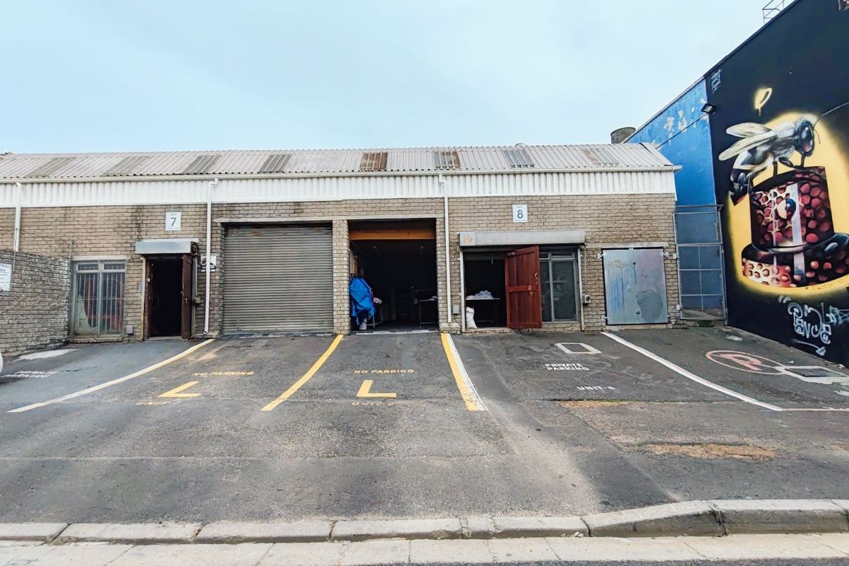 Front elevation of a commercial industrial unit featuring roller shutter access, dedicated parking bays, and a corrugated roof structure.