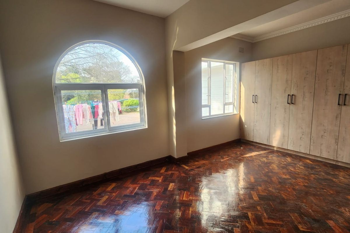 Spacious bedroom featuring classic parquet flooring, extensive built-in cupboards, and a distinctive arched window providing natural light.