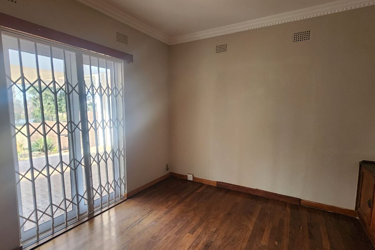 An empty living room featuring hardwood flooring, crown molding, and a sliding glass door with a security gate leading to the patio.