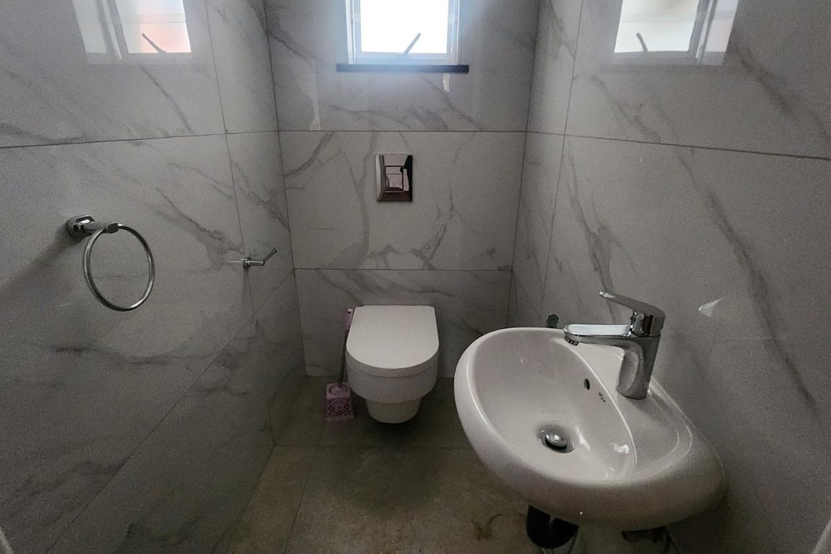 A modern, compact guest bathroom featuring marble-effect wall tiling, a wall-mounted toilet, and a sleek basin with a chrome mixer tap.