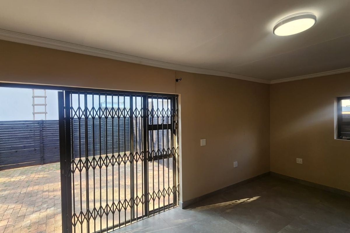 An empty living room featuring tiled flooring, a sliding door with a security gate, and access to an outdoor paved area.