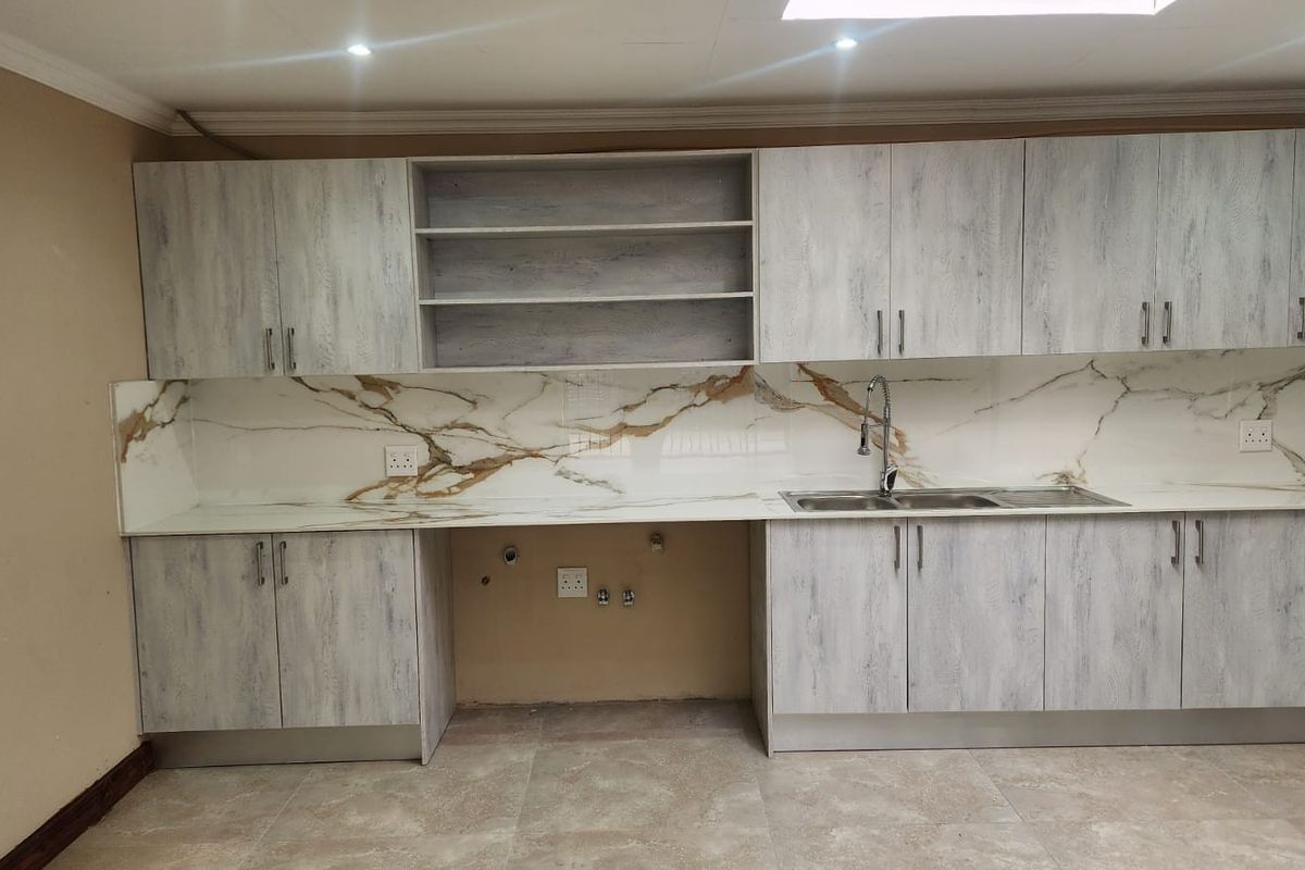 A modern kitchen featuring light wood-grain cabinetry, a marble-effect splashback, and a stainless steel sink, with dedicated space for under-counter appliances.