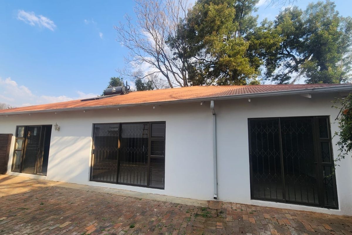 Rear exterior view of the house featuring a corrugated metal roof with a solar water heater, sliding glass doors with security gates, and brick paving.