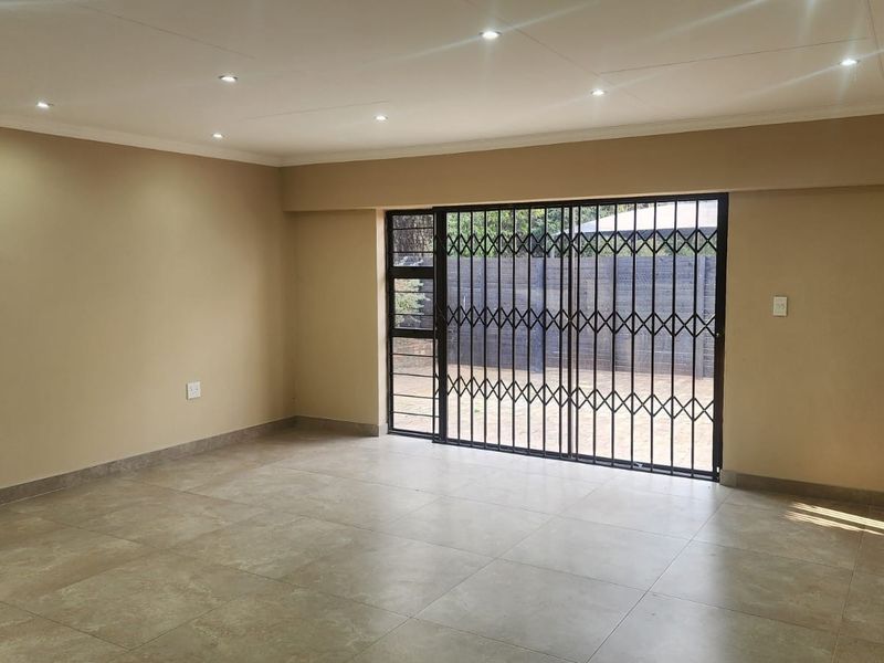 Spacious, empty living area featuring neutral tiled flooring, recessed downlighting, and a secure sliding glass door leading to the exterior.