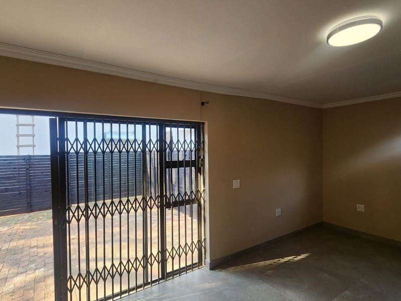 An empty living room featuring tiled flooring, a sliding door with a security gate, and access to an outdoor paved area.