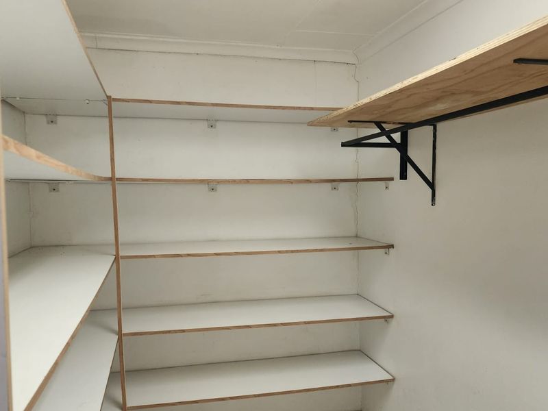 A functional walk-in pantry or scullery area featuring extensive built-in shelving units with metal support brackets.