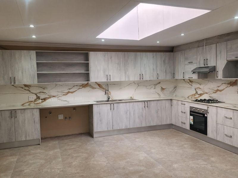 Modern kitchen featuring light wood-grain cabinetry, marble-look splashbacks, integrated appliances, and a large skylight providing ample natural light.