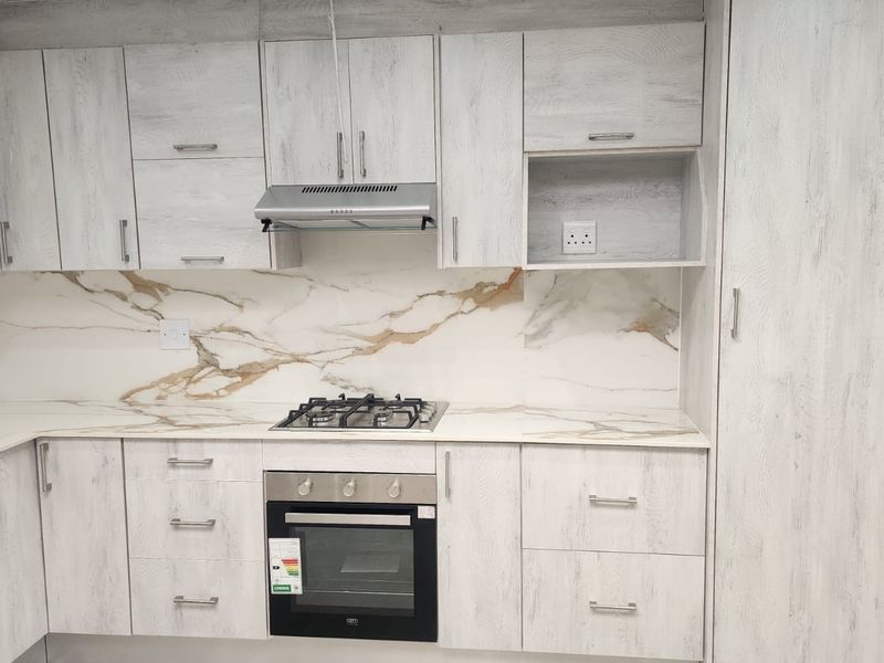 Modern kitchen featuring light wood-grain cabinetry, marble-effect splashback, integrated gas hob, built-in oven, and extractor fan.