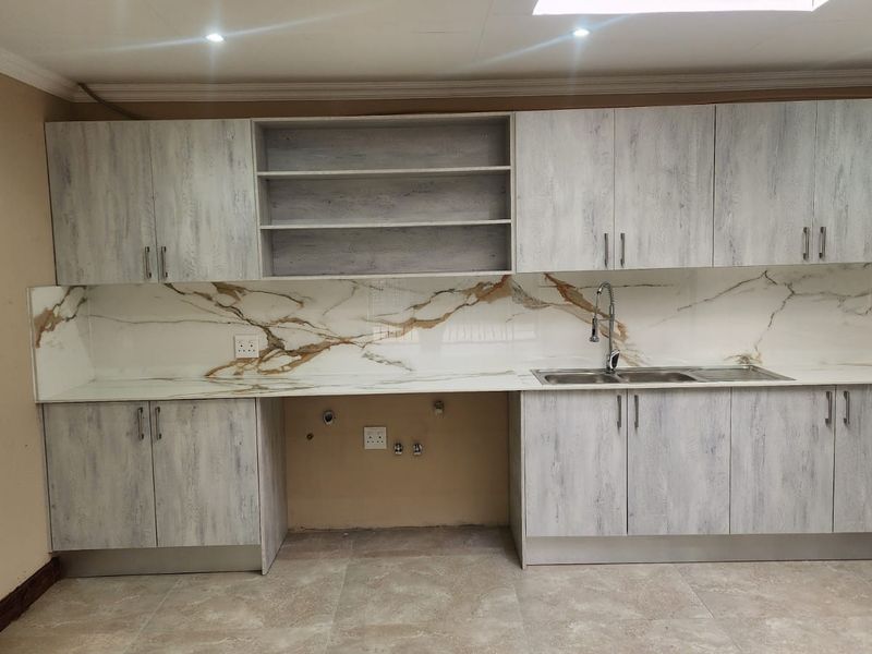 A modern kitchen featuring light wood-grain cabinetry, a marble-effect splashback, and a stainless steel sink, with dedicated space for under-counter appliances.
