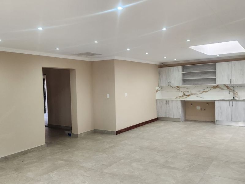 Spacious open-plan area featuring modern tiled flooring, recessed lighting, a skylight, and a contemporary kitchen with marble-look splashback and ample fitted cabinetry.