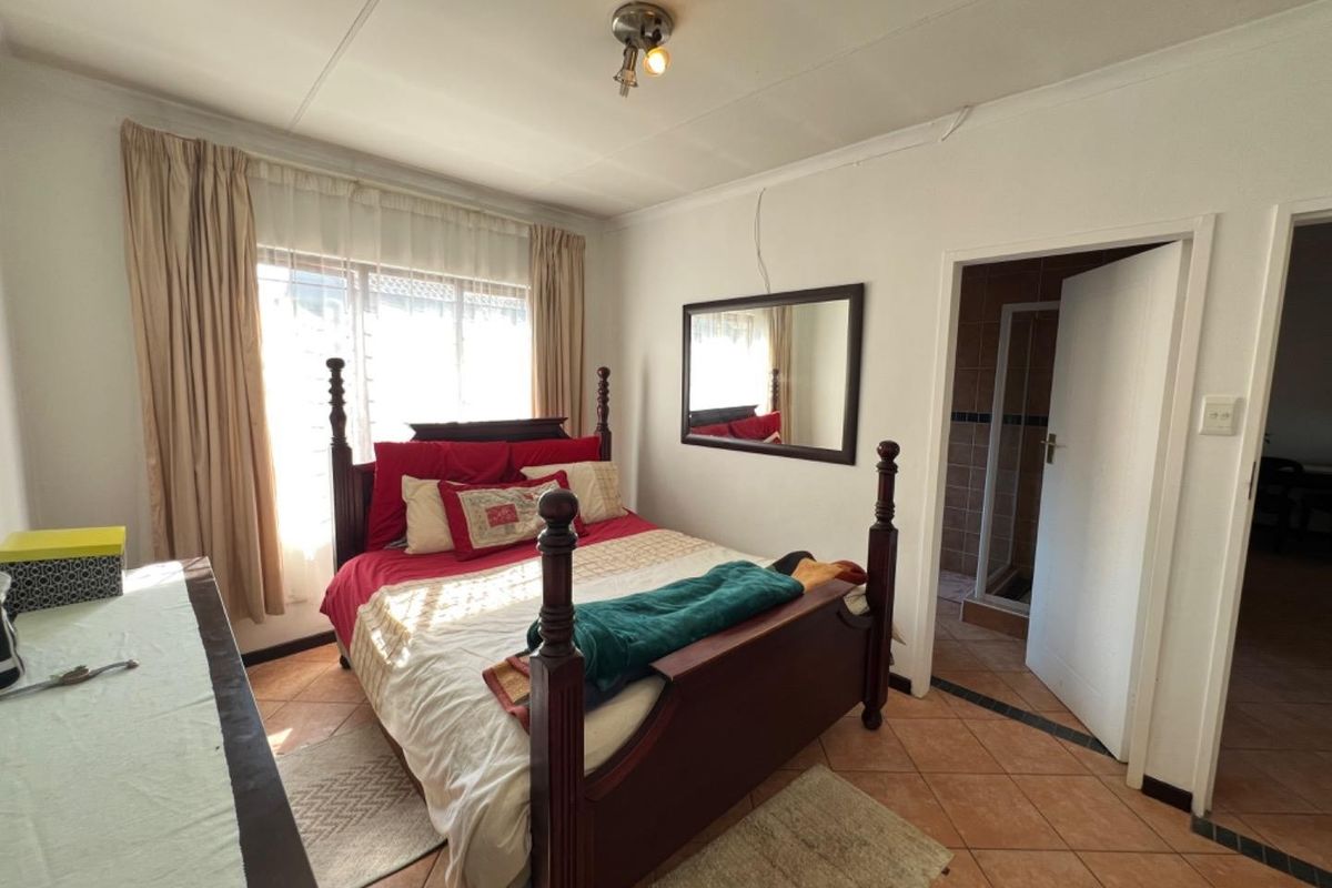 A bedroom featuring tiled flooring and direct access to an en-suite bathroom, with neutral wall finishes and natural light from the window.