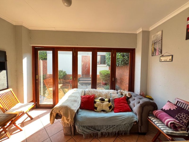 A sunlit living room featuring timber folding doors that open onto a private rear courtyard, finished with tiled flooring and coved cornicing.