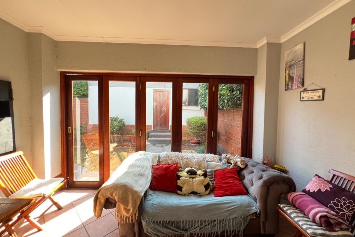 A sunlit living room featuring timber folding doors that open onto a private rear courtyard, finished with tiled flooring and coved cornicing.