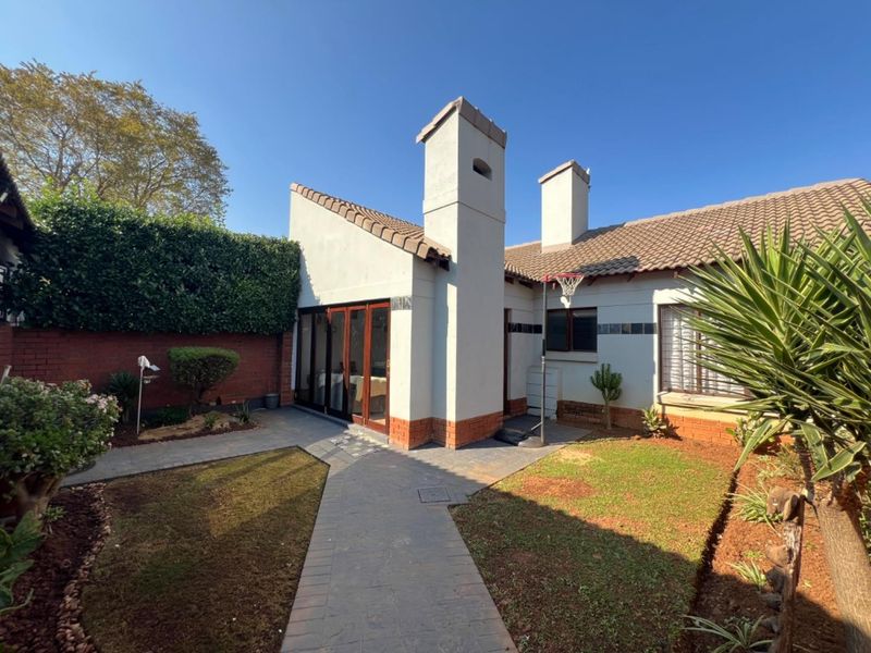 Rear view of the townhouse featuring a paved walkway, small garden area, brick boundary wall, and prominent chimneys.