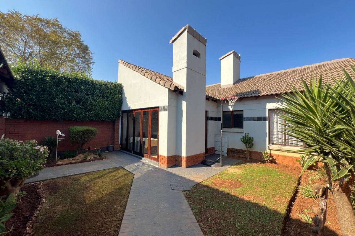 Rear view of the townhouse featuring a paved walkway, small garden area, brick boundary wall, and prominent chimneys.