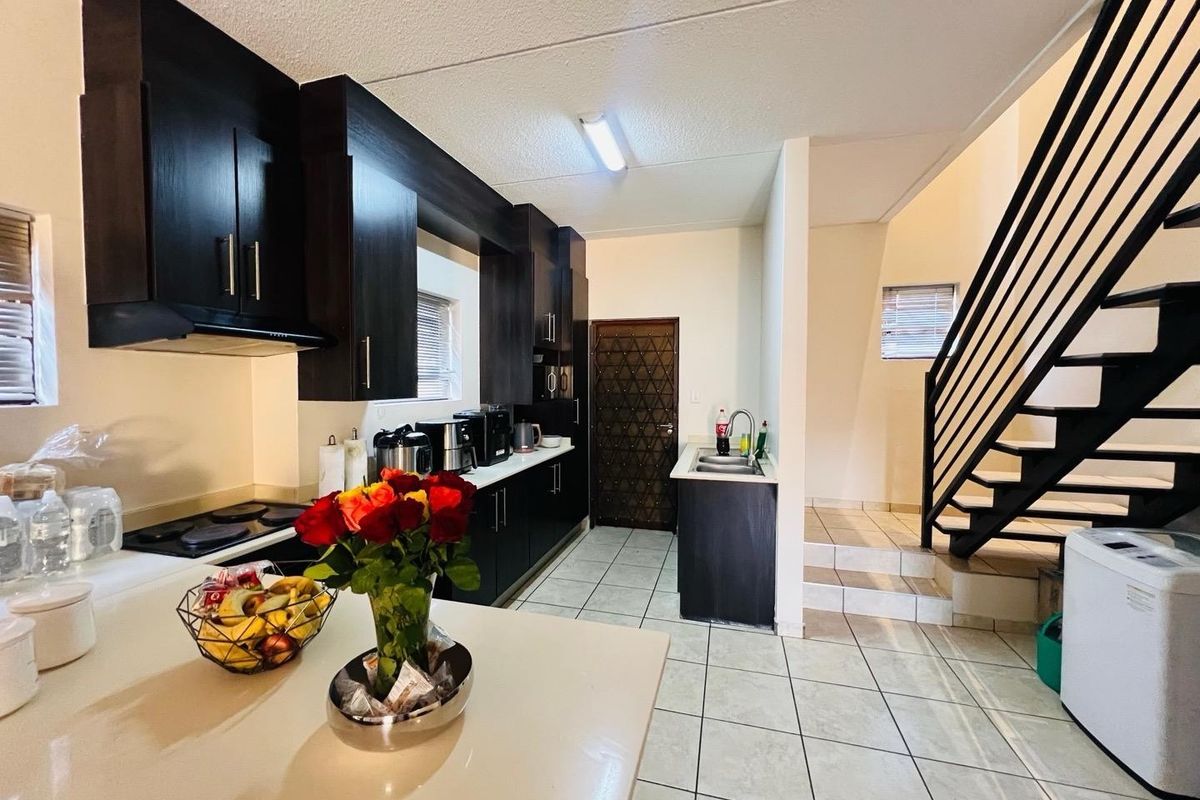 A functional kitchen featuring dark wood cabinetry, built-in hob, extractor fan, and tiled flooring, adjacent to an internal staircase.