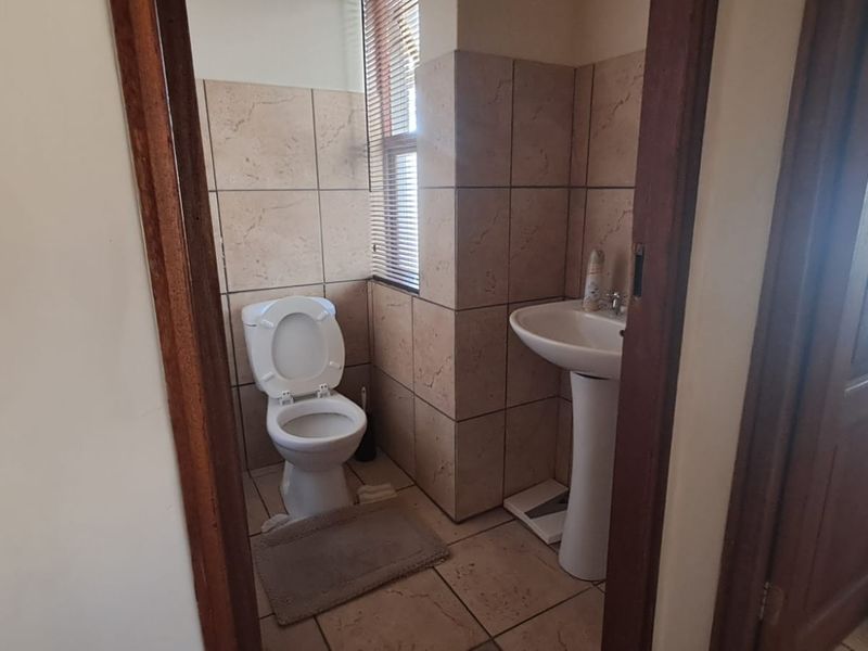 A functional bathroom featuring a pedestal basin, toilet, and neutral floor-to-ceiling wall tiling.