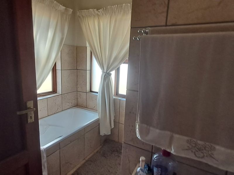 A functional bathroom featuring a built-in bathtub surrounded by neutral ceramic wall tiles and a wall-mounted towel rail.