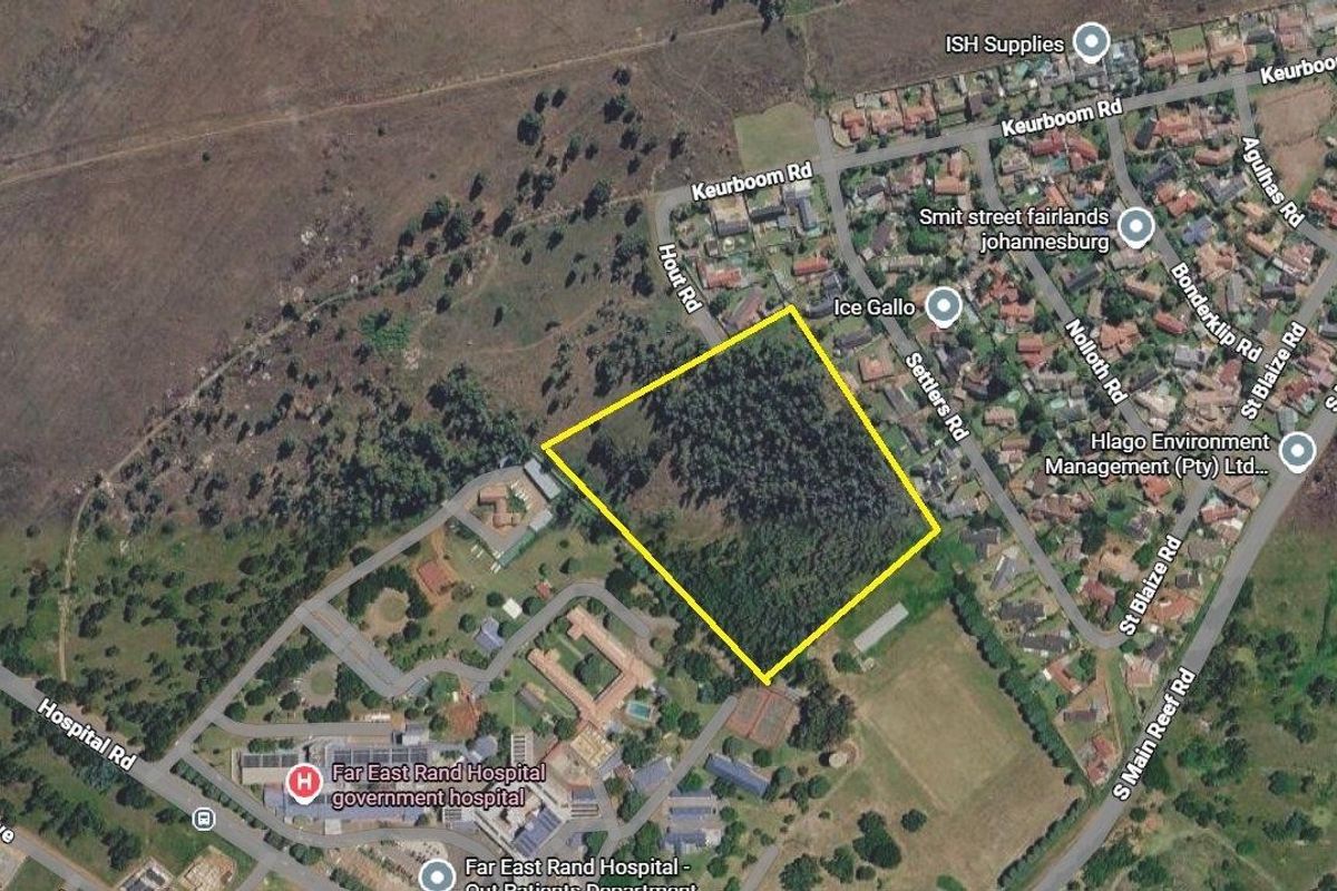 An aerial view of a vacant residential plot highlighted in yellow, situated in a suburban area near local infrastructure.