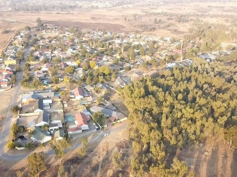 An aerial view of a residential neighborhood featuring established housing, paved street networks, and adjacent natural woodland areas.