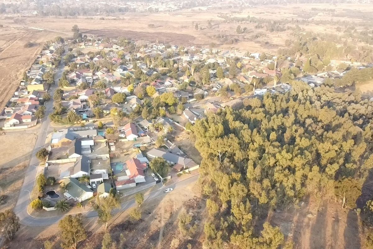 An aerial view of a residential neighborhood featuring established housing, paved street networks, and adjacent natural woodland areas.