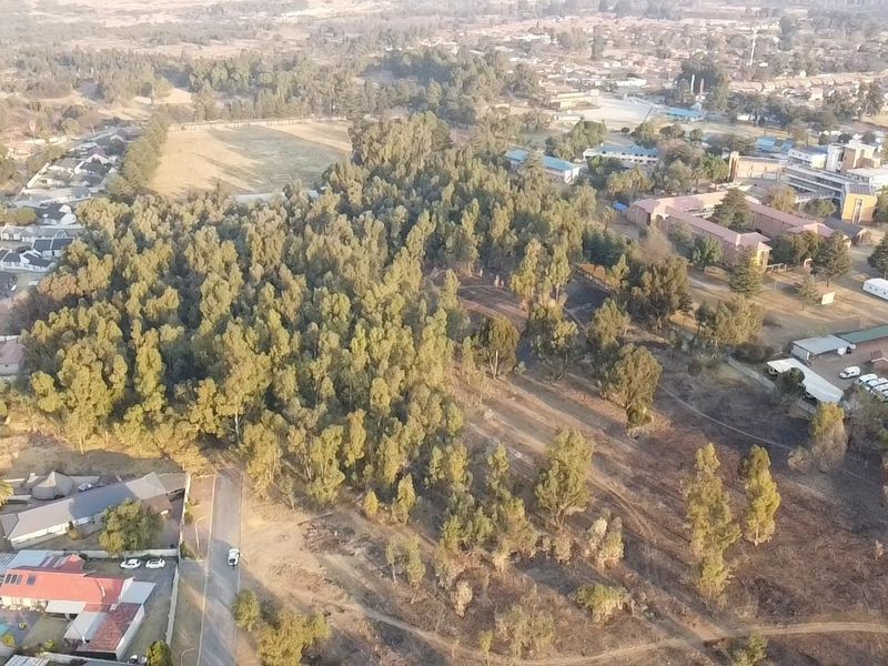 An aerial view of a large, partially wooded vacant residential plot situated within an established suburban neighborhood.