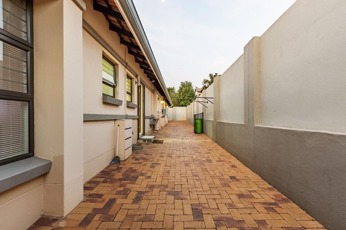A clean, paved side walkway along the exterior of the house, featuring a high boundary wall and well-maintained exterior finishes.