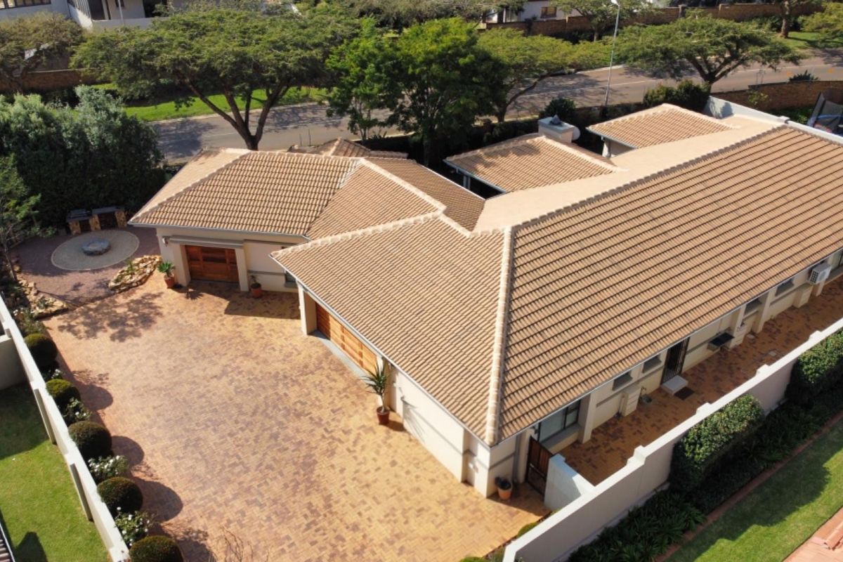 Aerial view of a residential property featuring a tiled roof, extensive paved driveway, and secure boundary walls.