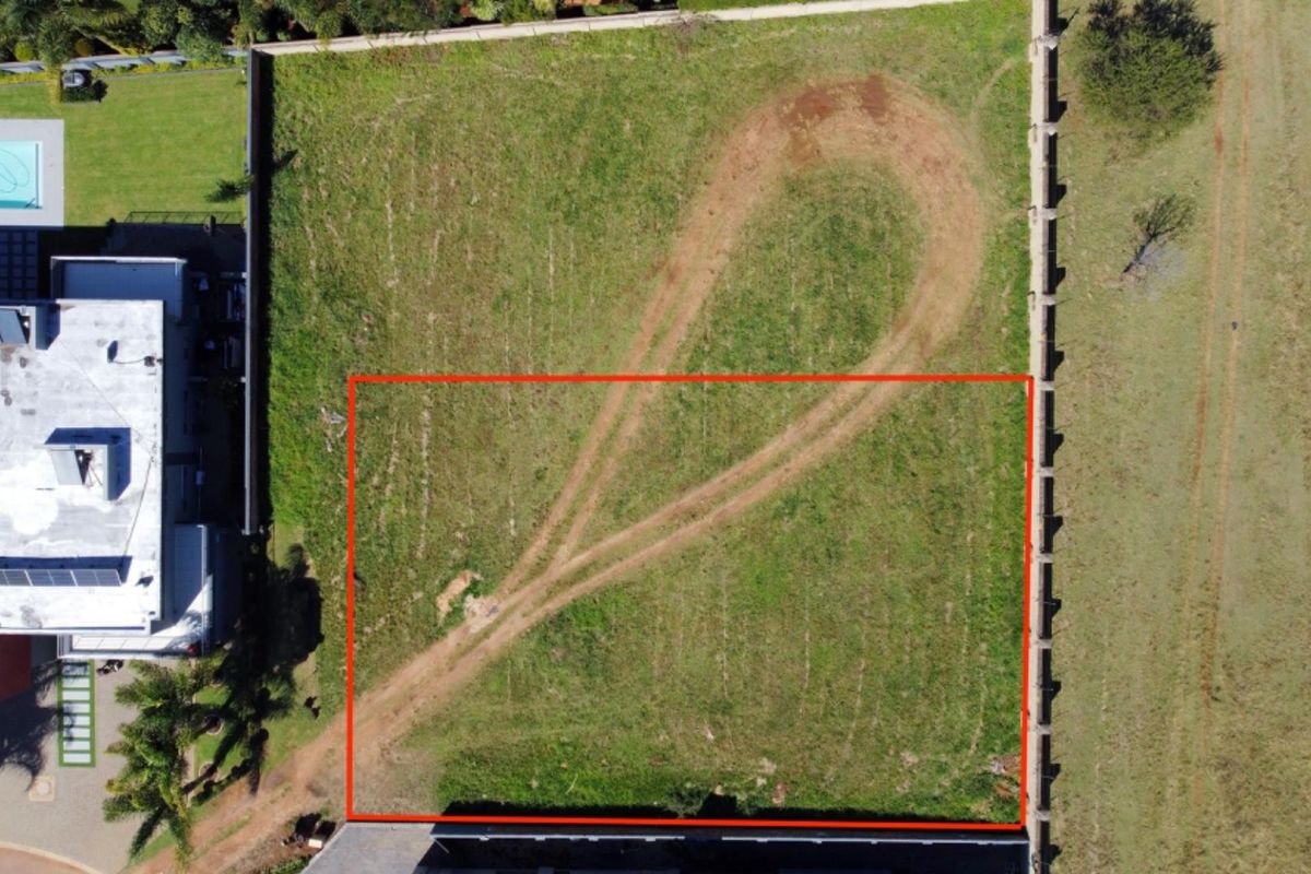 Aerial view of a vacant residential plot featuring grass cover and perimeter boundary walls, suitable for future development.