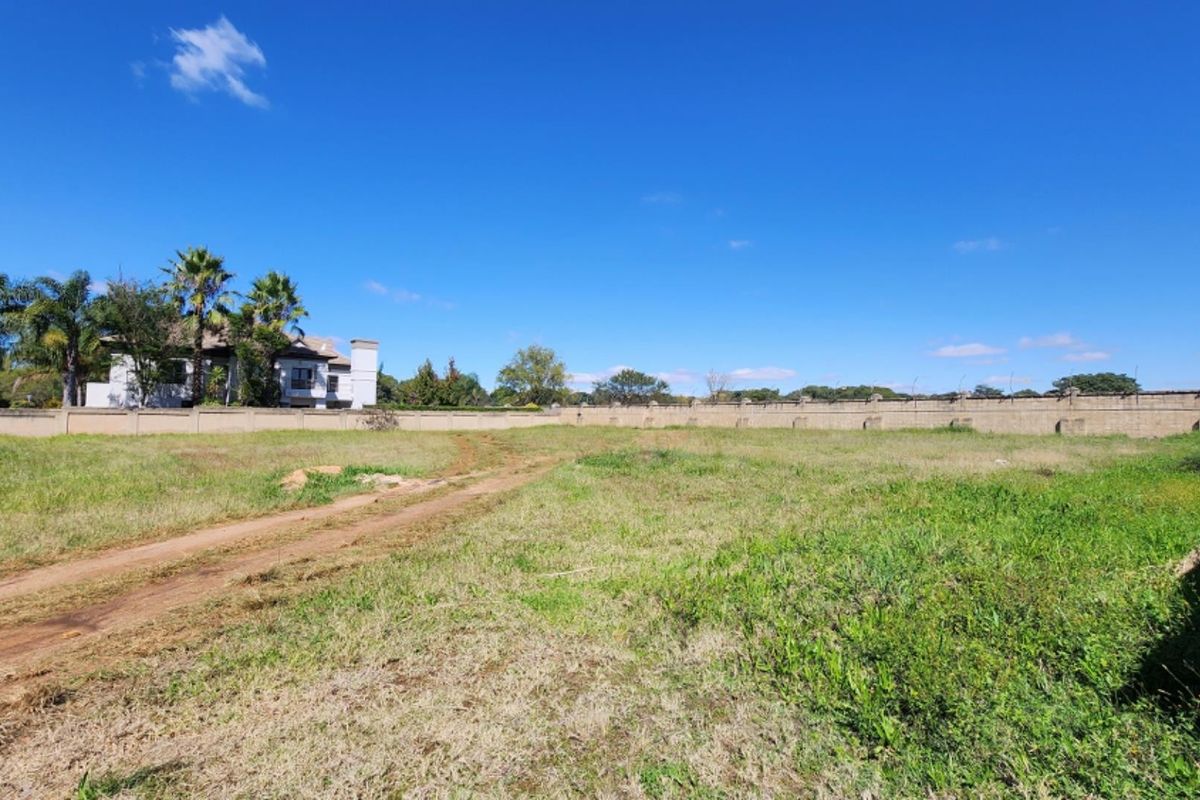 A wide-angle view of a vacant residential plot featuring a perimeter wall, security fencing, and an unpaved access track.