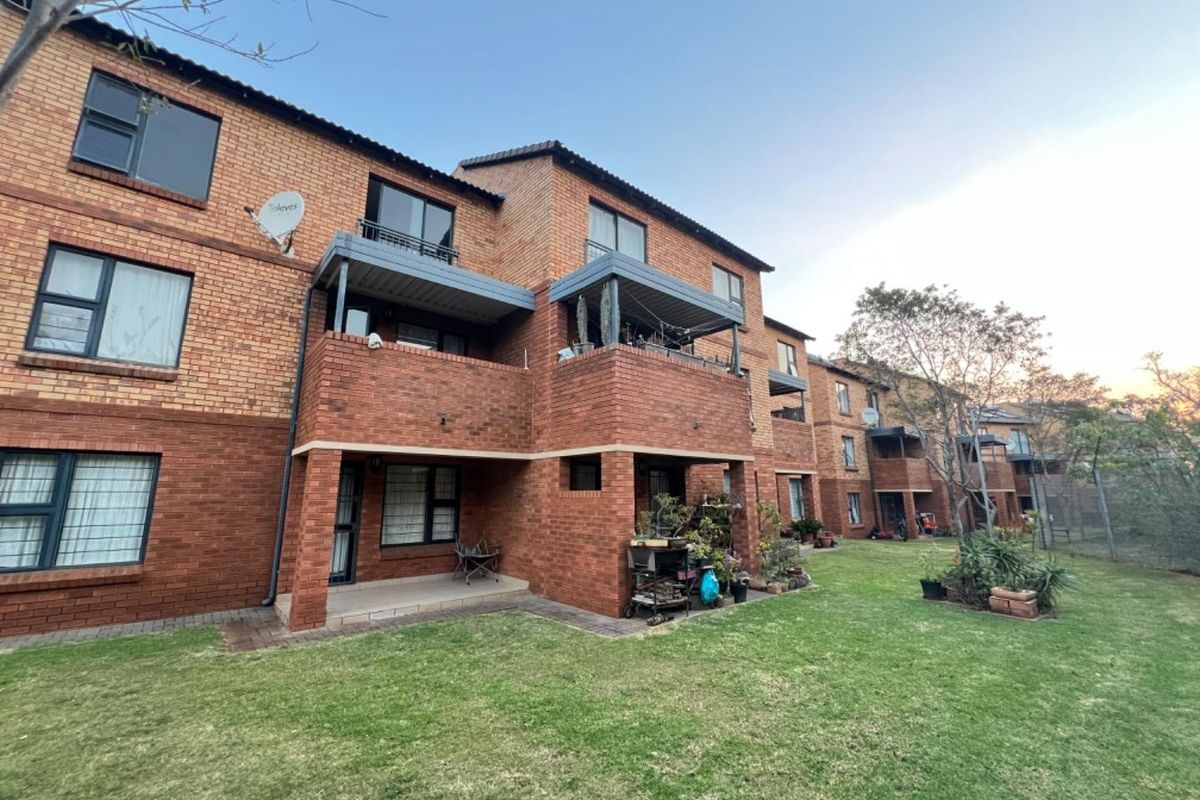 Rear view of a multi-story apartment complex featuring face brick construction, private balconies, ground-floor patios, and a well-maintained communal garden area.