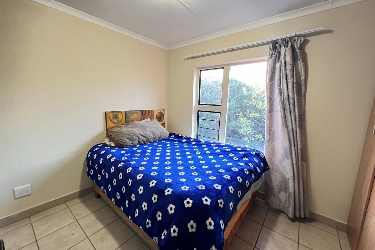 A functional bedroom featuring tiled flooring, a sliding window with natural light, and neutral wall finishes.