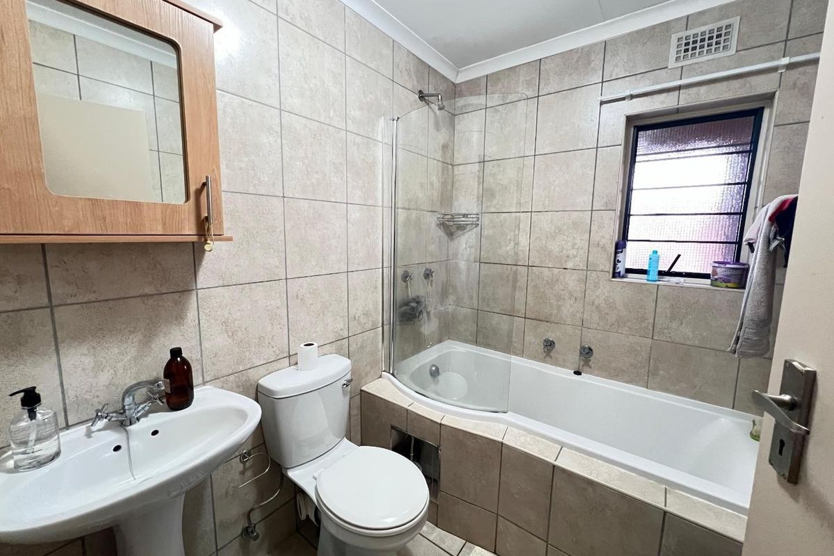 A functional bathroom featuring a pedestal basin, toilet, and a bathtub with a glass shower screen, finished with neutral wall and floor tiles.