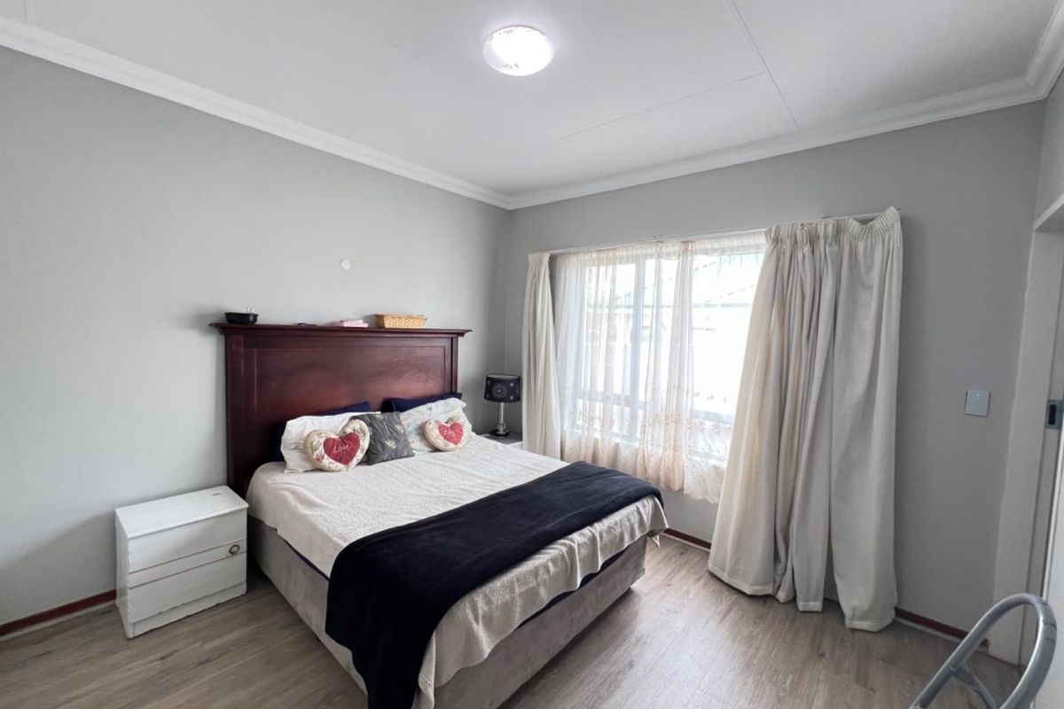 A well-maintained bedroom featuring light-toned laminate flooring, neutral wall finishes, and a large window with curtain tracks.