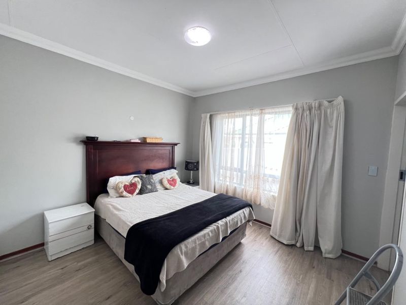 A well-maintained bedroom featuring light-toned laminate flooring, neutral wall finishes, and a large window with curtain tracks.