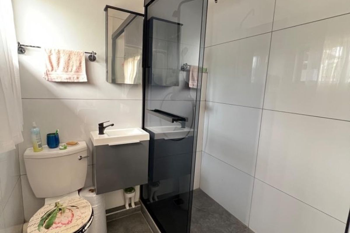 Modern bathroom featuring a walk-in shower with a black-framed glass screen, wall-mounted vanity, and neutral tiled finishes throughout.